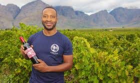 Tinashe Nyamudoka of Kumusha Wines in Zimbabwe stands with a bottle of his wine in his vineyard.