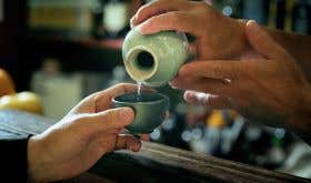 Sake being poured with two hands into a small celadon sake cup