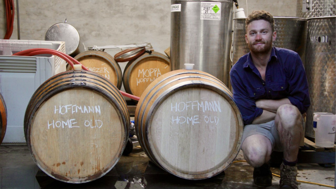 Winemaker Callum Powell kneeling next to his wine barrels