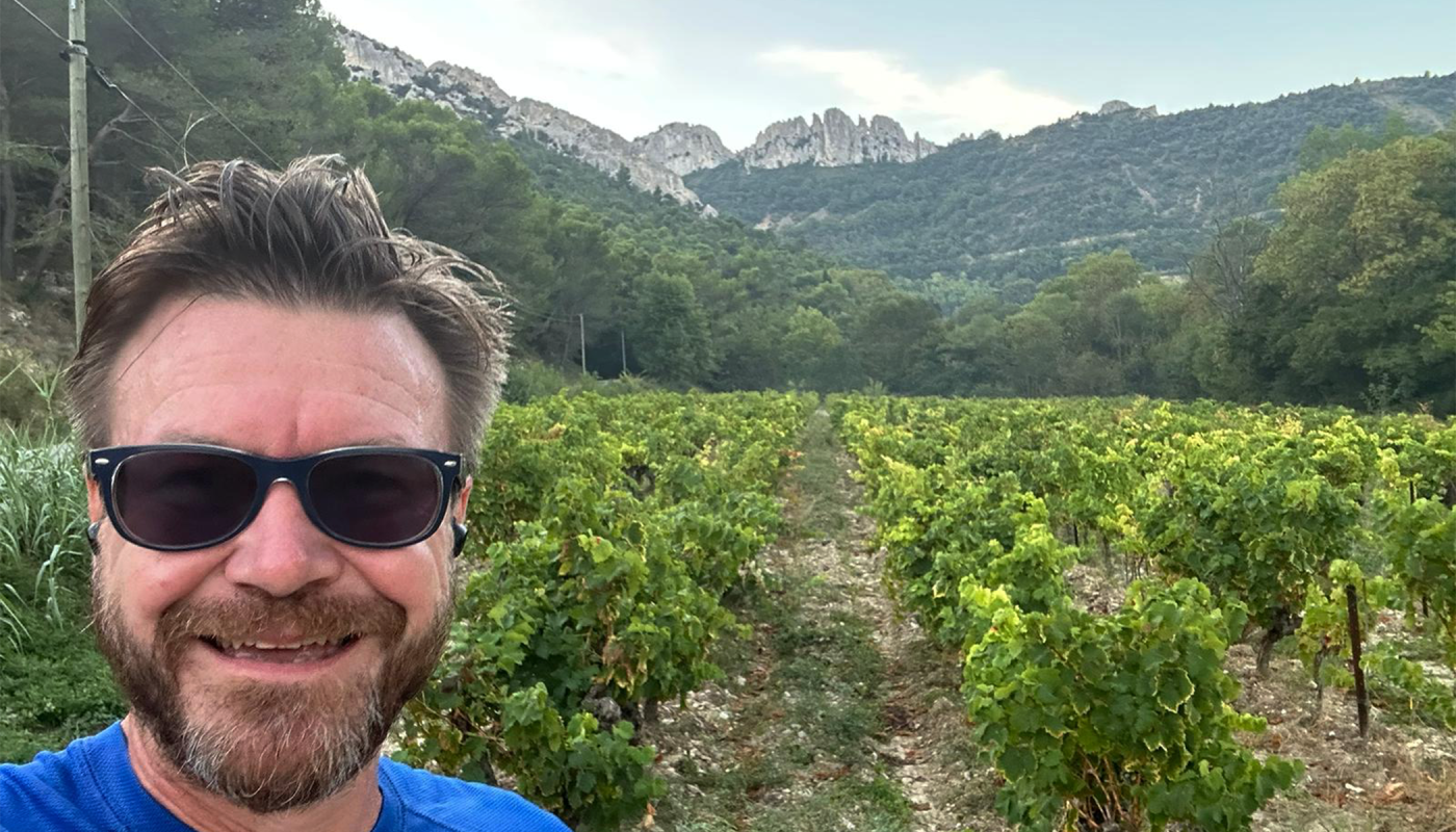 Les Dentelles rising up behind Ali as he stands in a vineyard in Gigondas