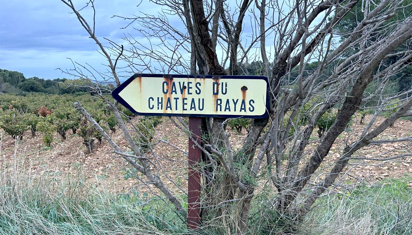 Sign pointing to Château Rayas winery, with vineyard in background.
