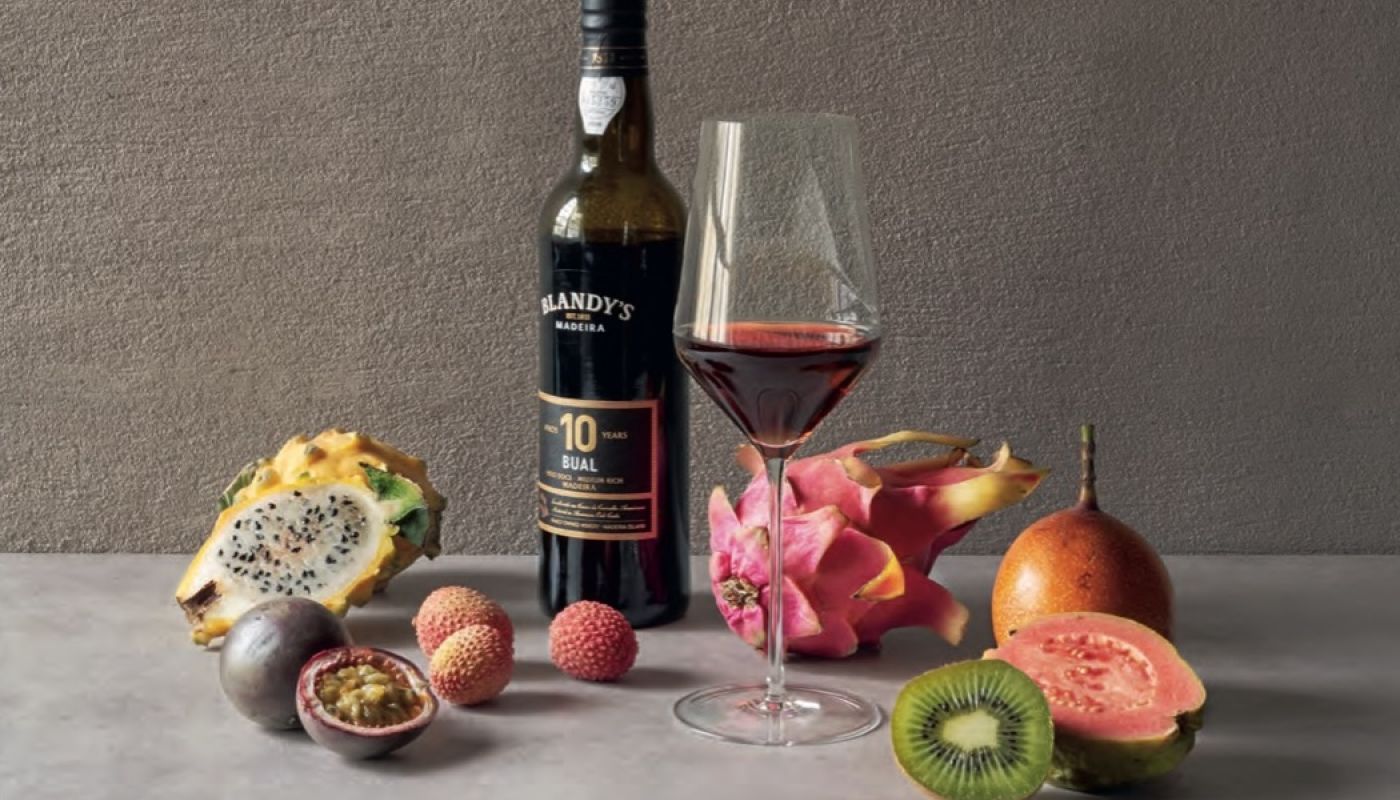 A bottle and glass of sweet Madeira surrounded by tropical fruits