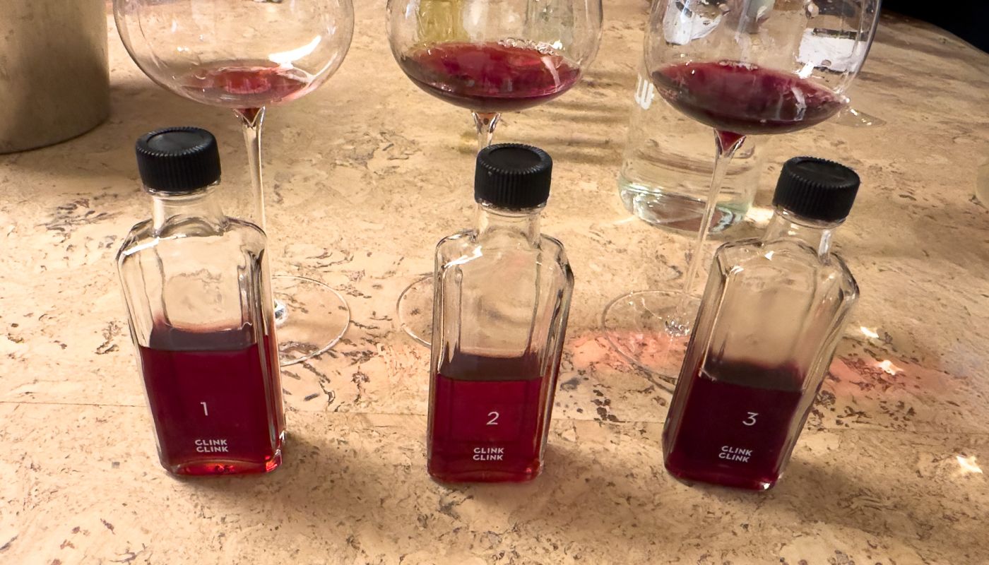 Three wine glasses and three miniature bottles, all containing small amounts of red wine