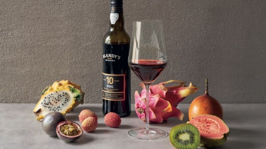 A bottle and glass of sweet Madeira surrounded by tropical fruits