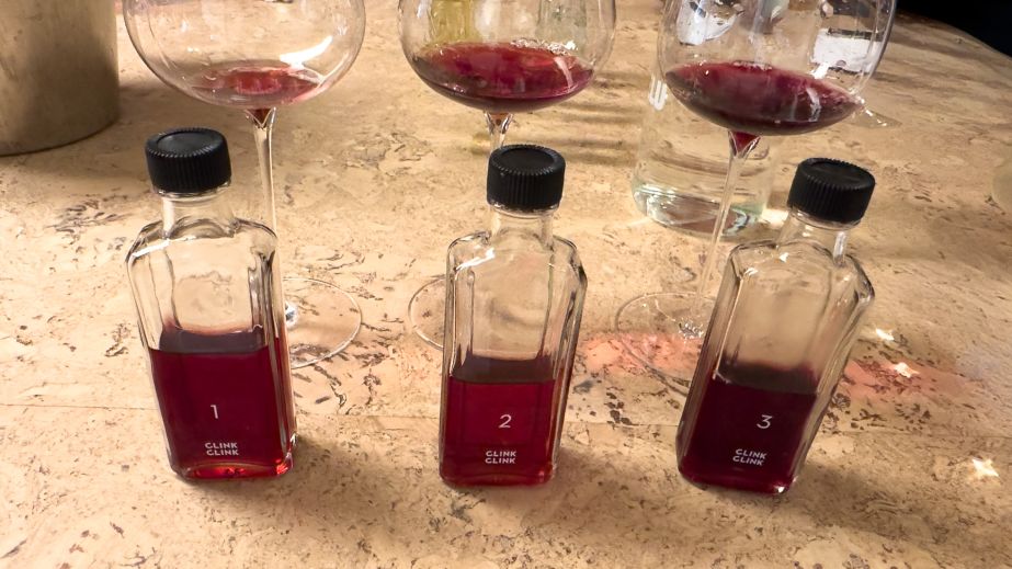 Three wine glasses and three miniature bottles, all containing small amounts of red wine