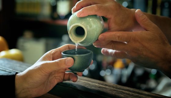 Sake being poured with two hands into a small celadon sake cup
