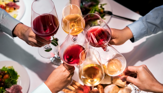 Classes of various-colored wines being clinked in cheers over a table; Credit Portra via Getty Images