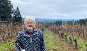 John Paul Cameron of of Cameron Winery in Oregon’s Willamette Valley stands in his vineyard holding a bottle of his wine.