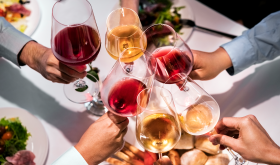 Classes of various-colored wines being clinked in cheers over a table; Credit Portra via Getty Images