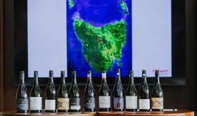 Bottles of Tasmanian wine standing in front of a screen showing a map of Tasmania