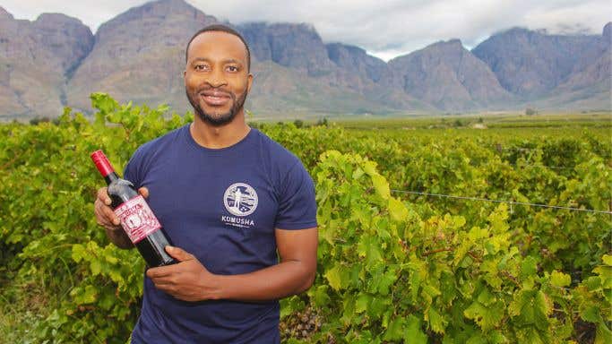 Tinashe Nyamudoka of Kumusha Wines in Zimbabwe stands with a bottle of his wine in his vineyard.