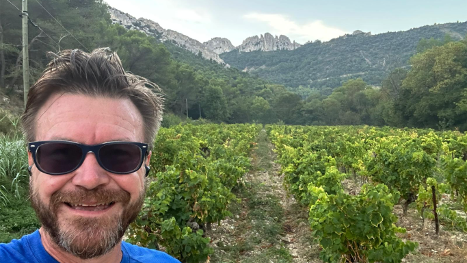 Les Dentelles rising up behind Ali as he stands in a vineyard in Gigondas