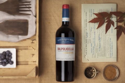 A promotional shot of a bottle of Valpolicella surrounded by spices, fruit, leaves and wooden cutlery.