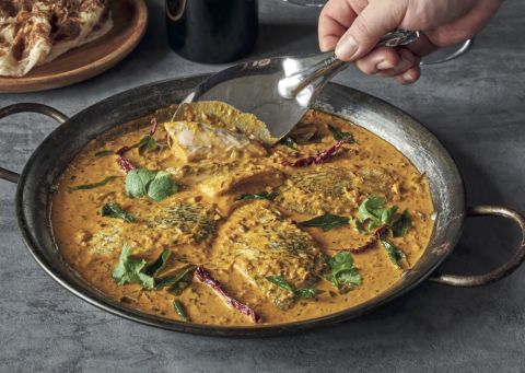 A fish curry in a wok, with a serving spoon held nearby