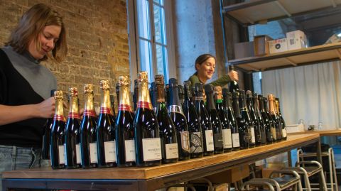Bottles of champagne lined up on a table, with Tara Q Thomas and Sam Cole-Johnson in the background