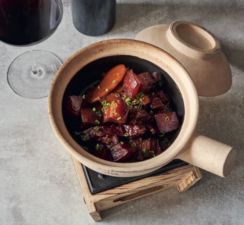 An overhead photo of red-braised pork in a round dish with a glass of red wine